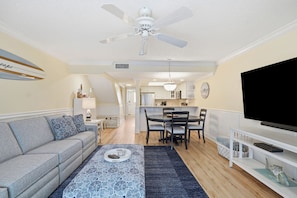 A living room with a sofa, coffee table, TV, and dining area with chairs and a table. - Seaside Escape - Private beach and pool! (St. Augustine Beach)