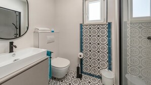 Un bagno con lavandino, WC e zona doccia, tutti in bianco.