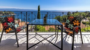 Un balcone con tavolo e sedie, vista sul mare e catena montuosa in lontananza.