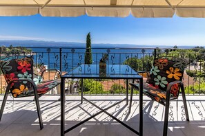 Ein Balkon mit Tisch und Stühlen, Blick auf das Meer und ein fernes Gebirge.