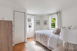 A bedroom with a bed, a nightstand, a lamp, a window with curtains, and a door. - Serene Cottage Near VA Wineries & Attractions (Paeonian Springs)