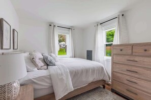 Ein Schlafzimmer mit Bett, Kommode und einem Fenster mit Vorhängen.