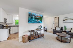 Ein modernes Wohnzimmer mit Flachbildfernseher, Couchtisch, Sofa und einem Essbereich mit Blick auf die Küche.