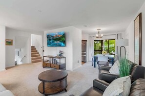 Ein Wohnzimmer mit Sofa, Couchtisch und Fernseher. Eine Treppe führt in einen anderen Raum.
