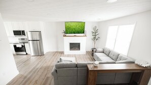 Una sala de estar moderna con un sofá seccional, una mesa de centro de madera, una chimenea y un televisor sobre ella.