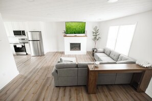 Una sala de estar moderna con un sofá seccional, una mesa de centro de madera, una chimenea y un televisor sobre ella.