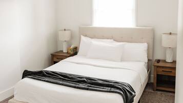 A bedroom with a bed, nightstands, a window, and a wall-mounted TV.