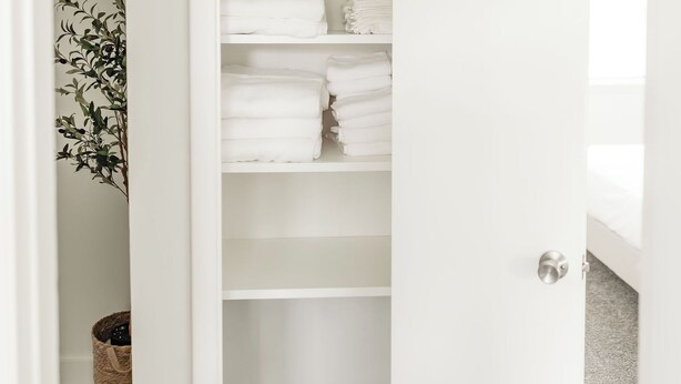Ein weißer Kleiderschrank mit Regalen, auf denen gefaltete Handtücher liegen.