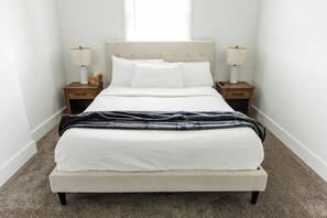 A bedroom with a bed, two nightstands, two lamps, a window, and a carpeted floor.