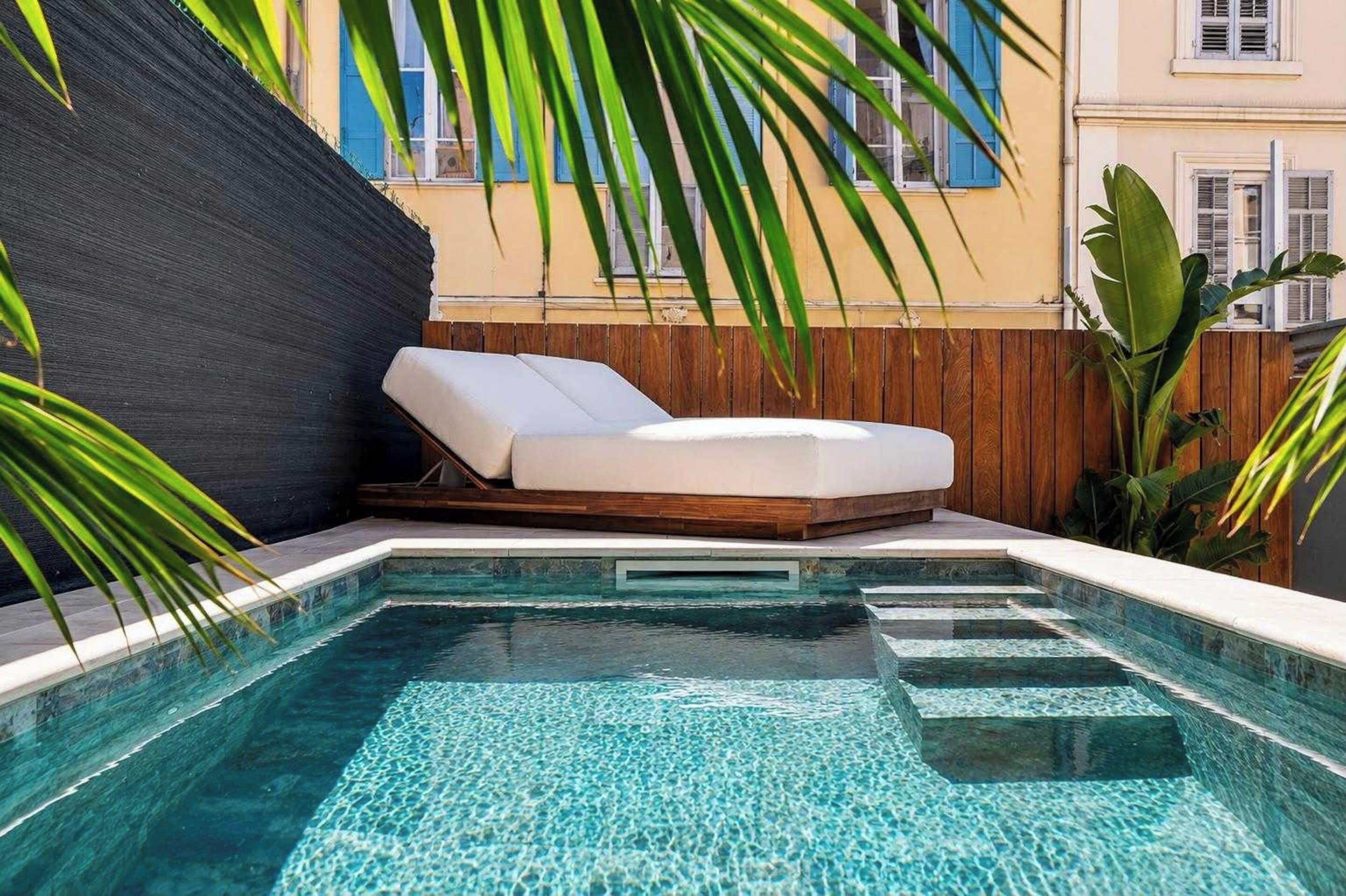 A poolside lounge area with a sun lounger, a clear pool, and a wooden fence.