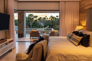 Ein Schlafzimmer mit einem großen Bett, einem Fernseher, einer Sitzecke mit Blick auf Palmen und einen Pool.