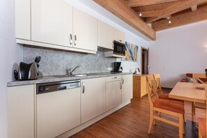 A modern kitchen with a dishwasher, microwave, and wooden dining table with chairs. - Klawunn Hotel & Apartement (Piesendorf)