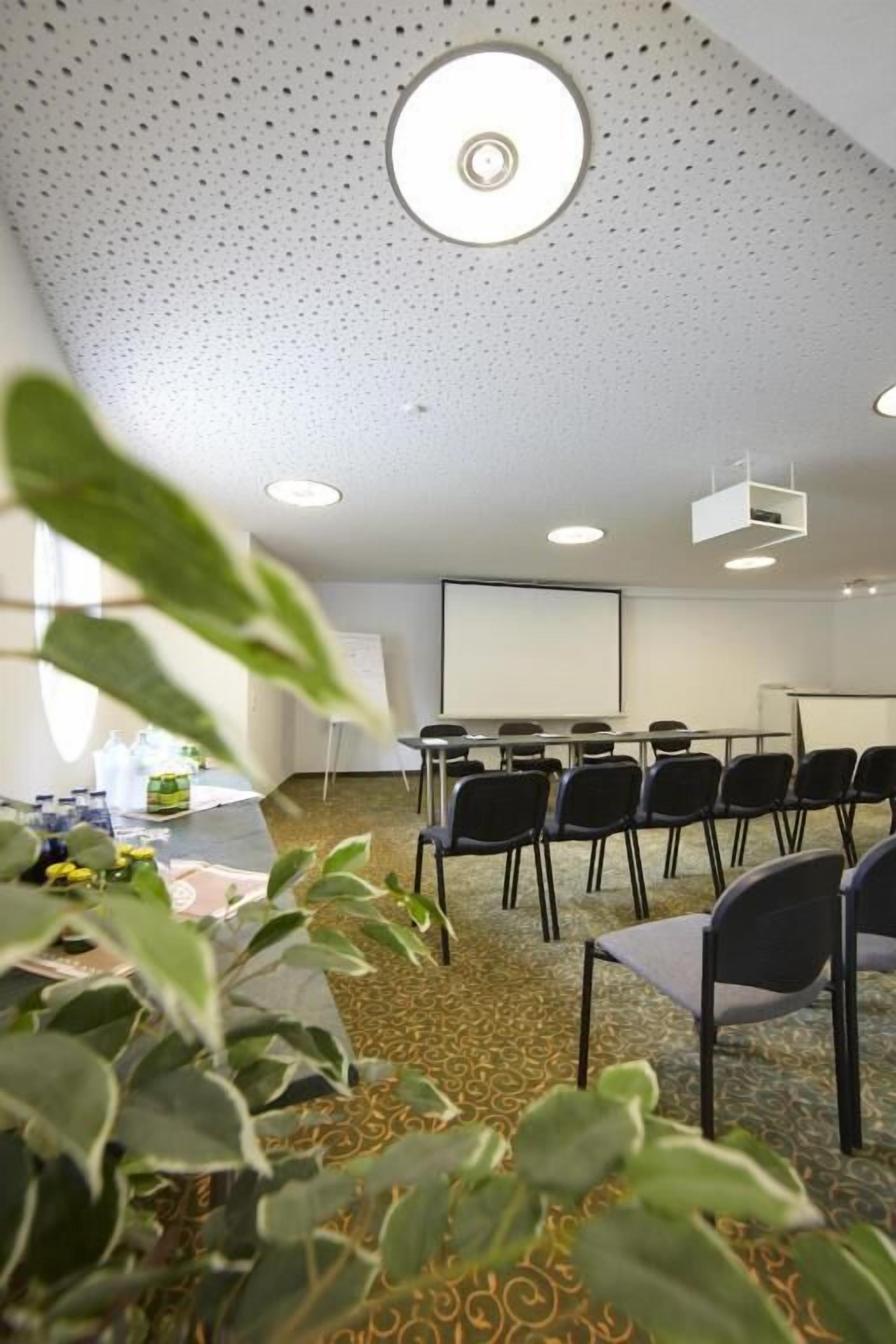 A conference room with a carpeted floor, a projector screen, and several chairs arranged around a table.