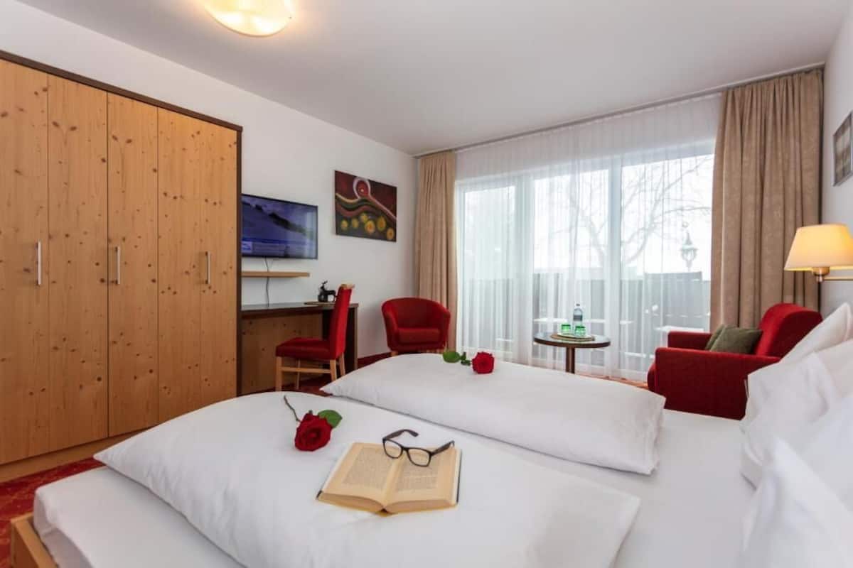 Una habitación de hotel con cama, escritorio, televisor, armario y ventana con cortinas.