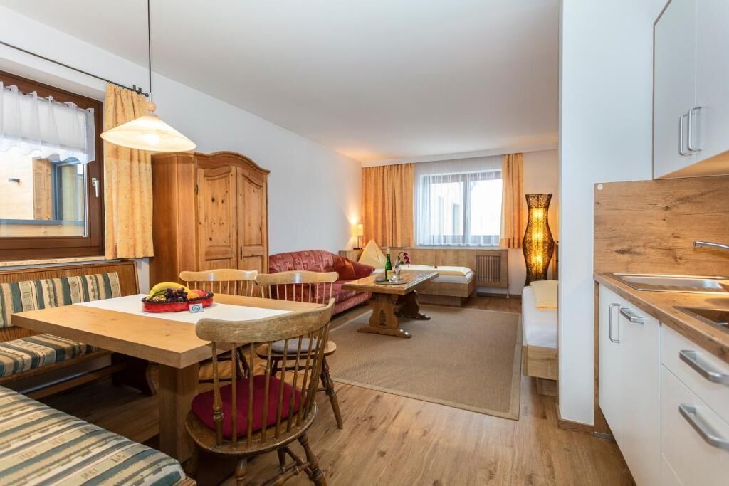 Una cocina compacta con armarios de madera, un comedor con mesa y sillas, y una zona de estar con sofá y banco.