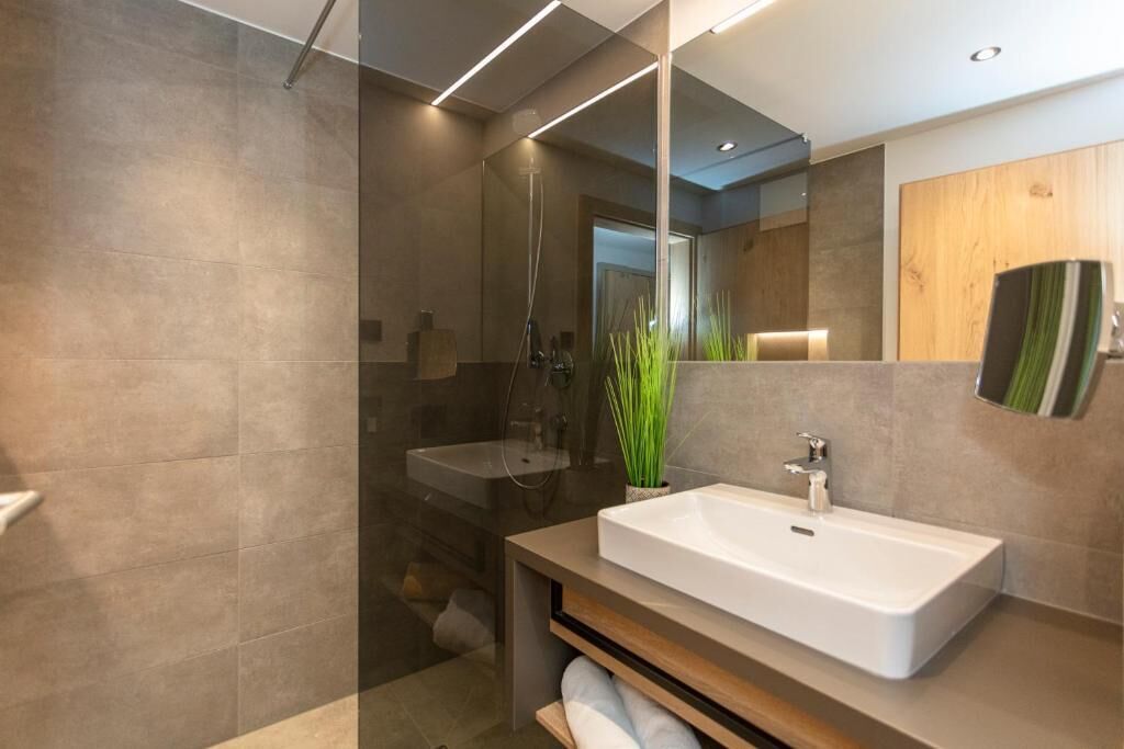 A modern bathroom with a large mirror, a rectangular sink, and a shower area.