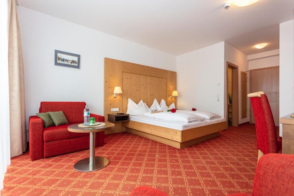 Una habitación de hotel con una cama, un sofá rojo, una mesita y un cabecero de madera.
