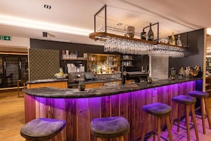 Zona de bar con mostrador curvo, taburetes y botelleros.