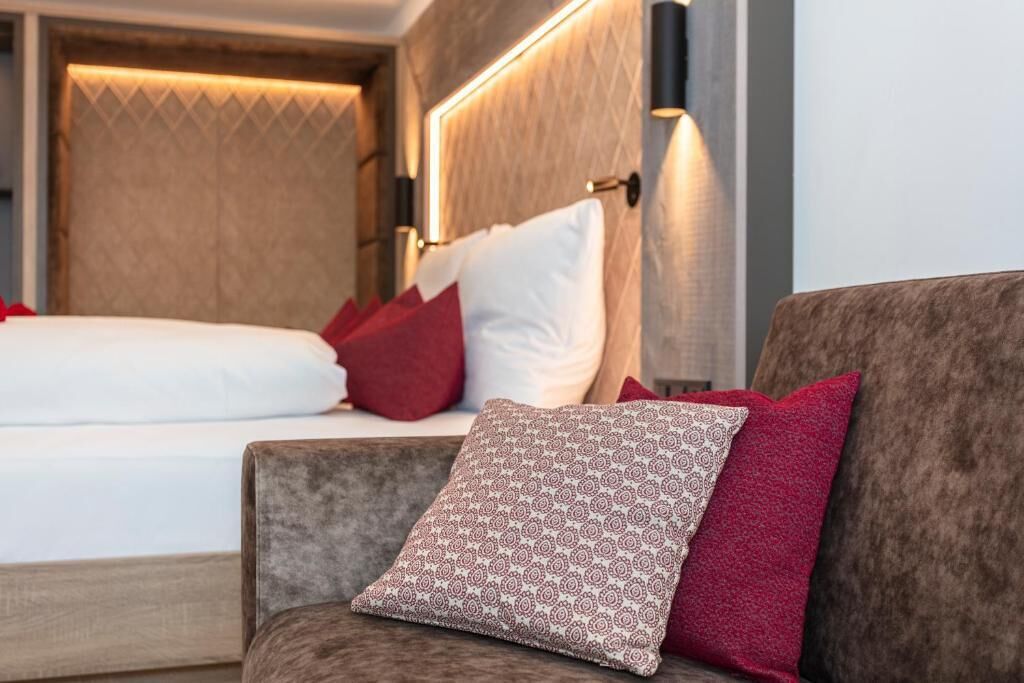 Habitación de hotel con cama, sofá, almohadas estampadas y una lámpara fijada a la pared.