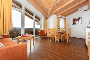 Amplia sala de estar con techo de madera, una mesa de comedor con sillas, un sofá y un tablero de ajedrez.