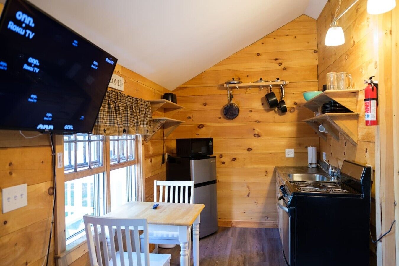 Une cuisine de taille réduite avec des murs en bois, un téléviseur fixé au mur, une cuisinière, un réfrigérateur et une fenêtre.