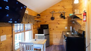Una cocina pequeña con paredes de madera, un televisor montado en la pared, una estufa, un refrigerador y una ventana.