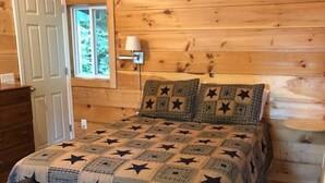 Una habitación con paneles de madera, una cama, un banco, una mesita de noche, una lámpara y una ventana.