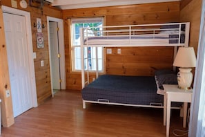 Een houten kamer met een stapelbed, een klein tafeltje met een lamp en een deur.