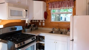 A kitchen with white cabinets, a microwave, a stove, a sink, and a window with a checkered valance.