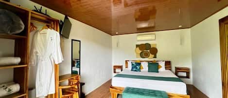 A bedroom with a wooden ceiling, a bed with a green blanket, a wooden bench, a wooden wardrobe, and a mirror.