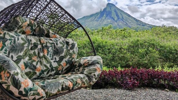 Una poltrona sospesa con tessuto a fantasia tropicale, una montagna sullo sfondo e un sentiero sterrato.