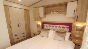 A bedroom with a large bed, wooden wardrobe, bedside tables, and a headboard with floral pattern. - Daletree View (Skipton)