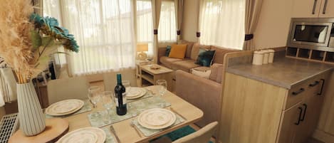 A dining area with a table set for four, a sofa, a kitchen area with a microwave, and a window with curtains.