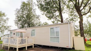 A mobile home with a patio, a small deck, and a window. - Daletree View (Skipton)