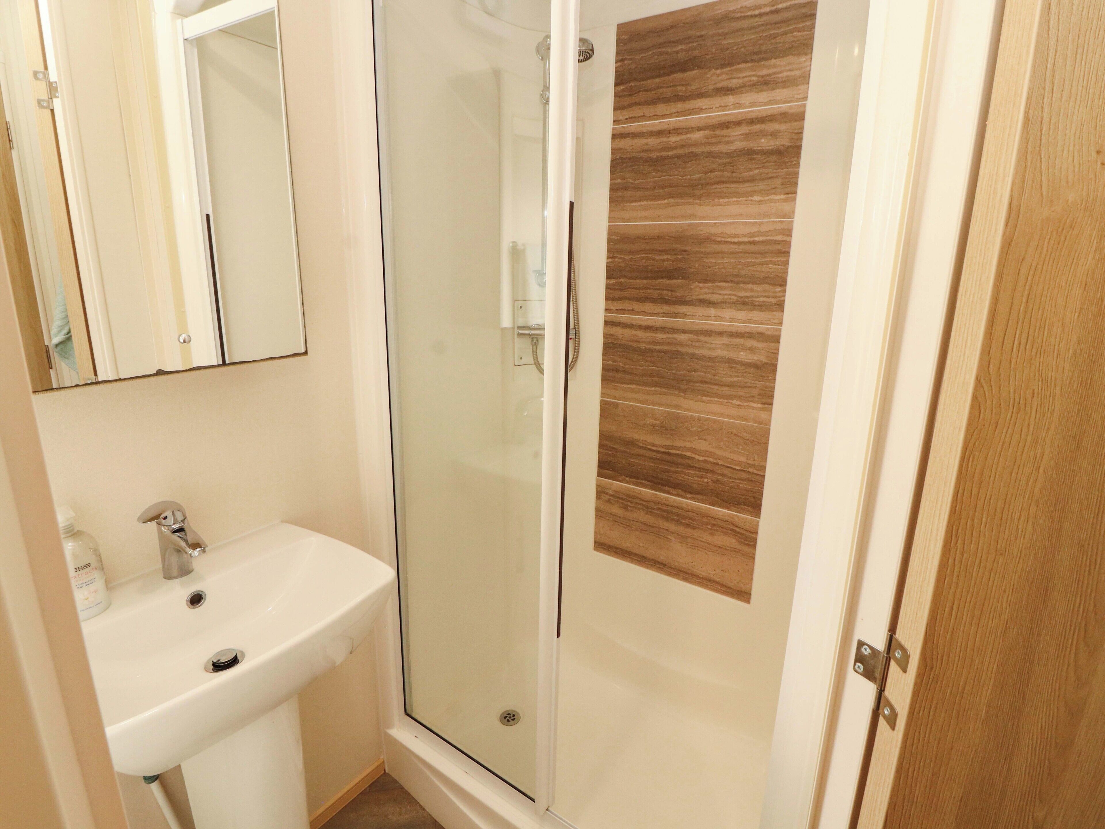 Une salle de bain avec une douche à parois de verre, un lavabo et un panneau en bois sur le mur.