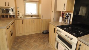 A compact kitchen with wooden cabinets, a built-in microwave, a gas stove, and a sink. - Daletree View (Skipton)
