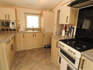 Eine kleine Küche mit Holzausstattung, einer eingebauten Mikrowelle, einem Gaskochfeld und einem Spülbecken.