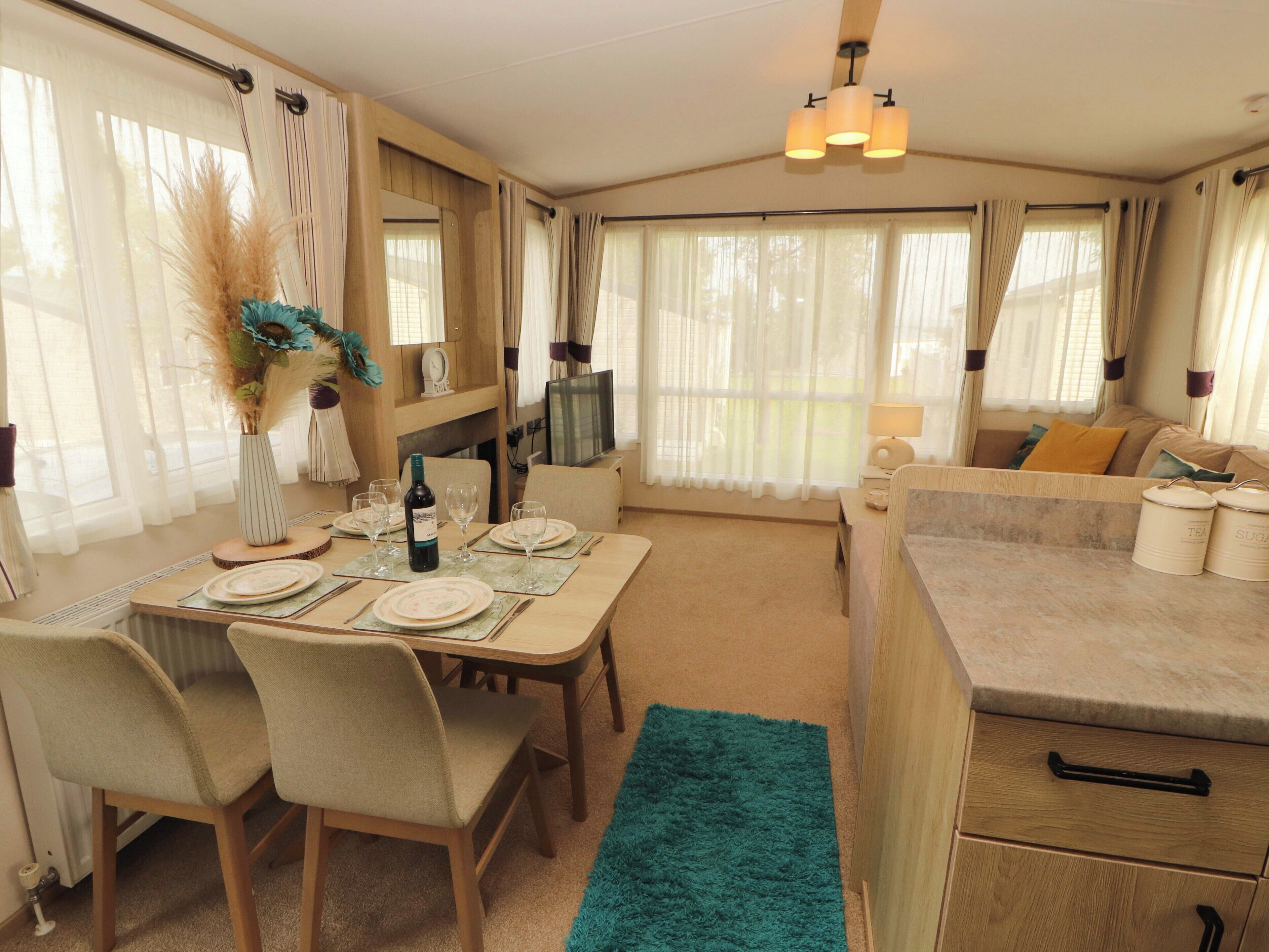A cozy RV interior with a dining area, kitchen, and large windows.
