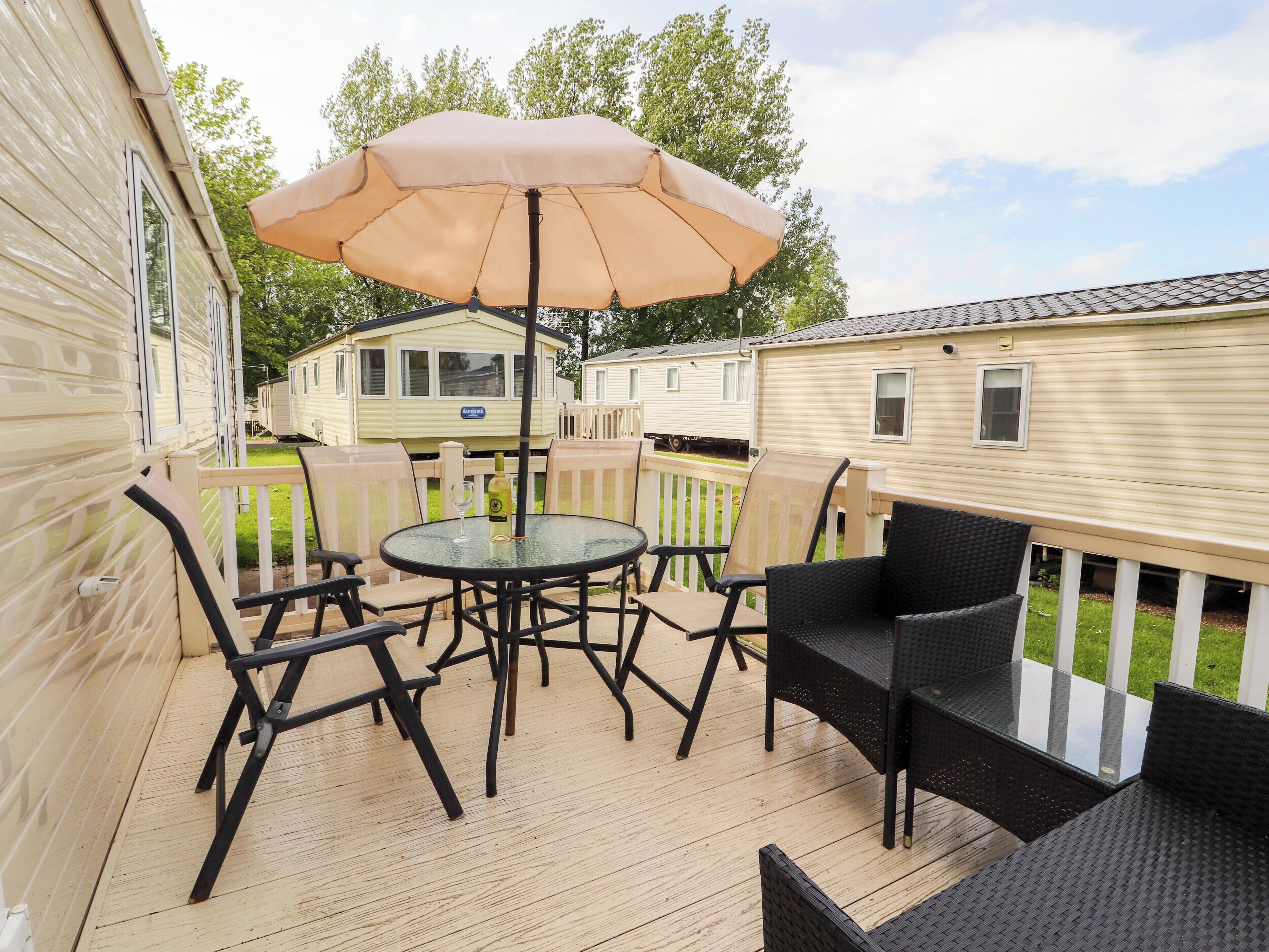 A deck with a table and chairs, an umbrella, and a bottle of wine.