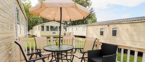 A deck with a table and chairs, an umbrella, and a bottle of wine.