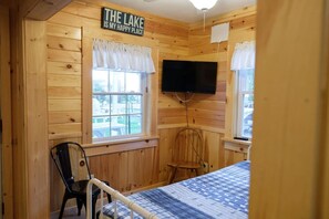 A cabin room with a bed, a chair, a television, and a sign that says 'THE LAKE IS MY HAPPY PLACE.' - Black Bear Cottage on the Stunning West Shore of Sebago Lake (Sebago)
