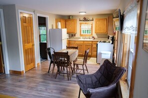 A compact kitchen with wooden cabinets, a dining table with chairs, and a refrigerator. - Salmon Cottage on the Stunning West Shore of Sebago Lake (Sebago)
