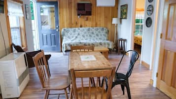 Una habitación acogedora con suelo de madera, un sofá, una mesa de comedor con sillas, un pequeño calentador y una puerta que da a otra habitación.