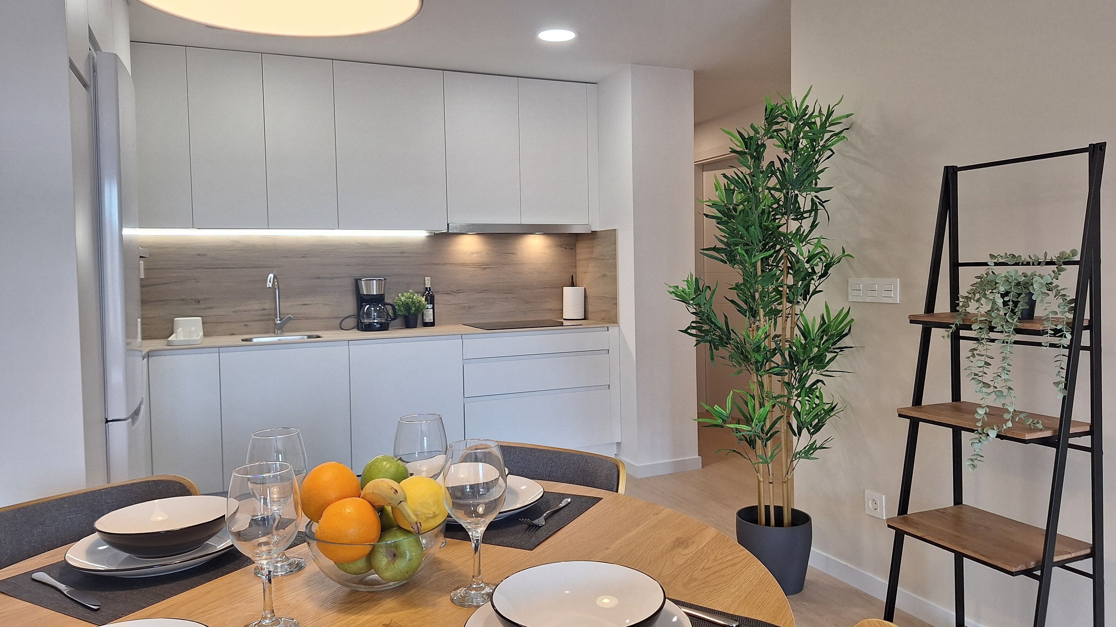 A modern kitchen with white cabinets, a wooden countertop, and a dining area with a table set for two.