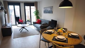 A modern living room with a dining area, a sofa, a coffee table, and a cityscape painting on the wall. - Apartamentos Plaza Costa 7 (Calatayud)