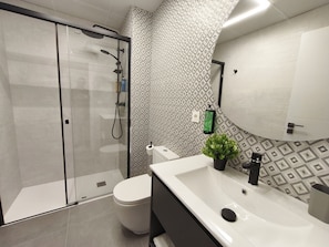 A modern bathroom with a glass-enclosed shower, a toilet, a sink with a black faucet, and a patterned wall. - Apartamentos Plaza Costa 7 (Calatayud)