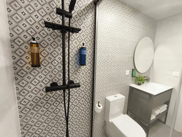 A bathroom with a patterned wall, a toilet, a sink with a mirror, and a shower area with a hose. - Apartamentos Plaza Costa 7 (Calatayud)