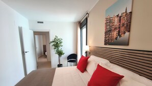 Una habitación de hotel con una cama, una planta en maceta, una silla, una ventana y un cuadro en la pared.