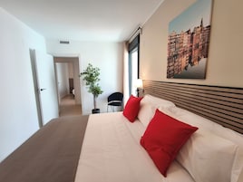 Una habitación de hotel con una cama, una planta en maceta, una silla, una ventana y un cuadro en la pared.