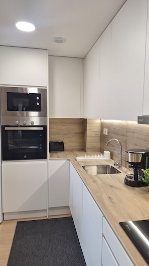 Una cocina moderna con armarios blancos, horno empotrado, tostadora, lavabo y cafetera.